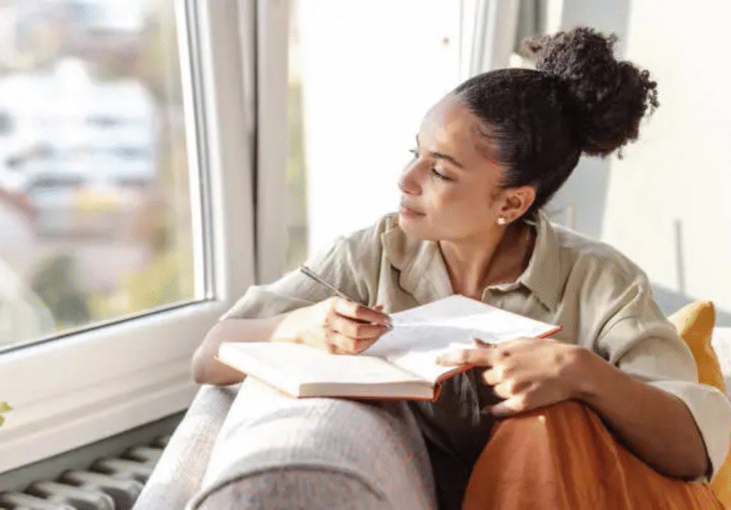 Woman sitting by a window writing in a journal while looking outside.Setting Boundaries: Know Your Worth and Choose Better