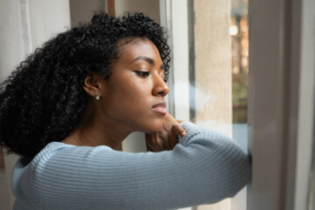 Woman looking out a window with a thoughtful, distant expression.