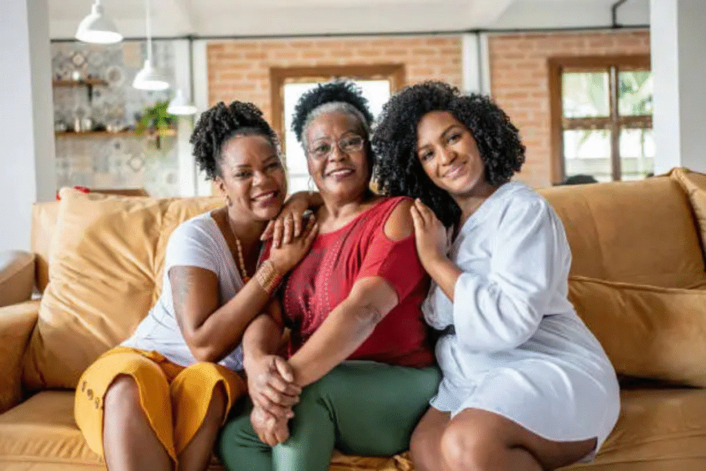Mother sitting with her two adult daughters on a couch, all smiling and close together.