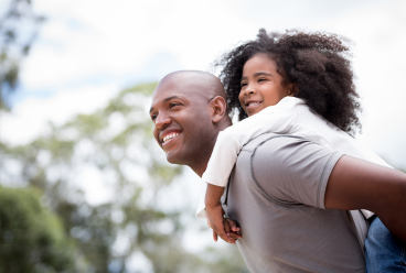 Man carrying a young girl on his back while they are outdoors.